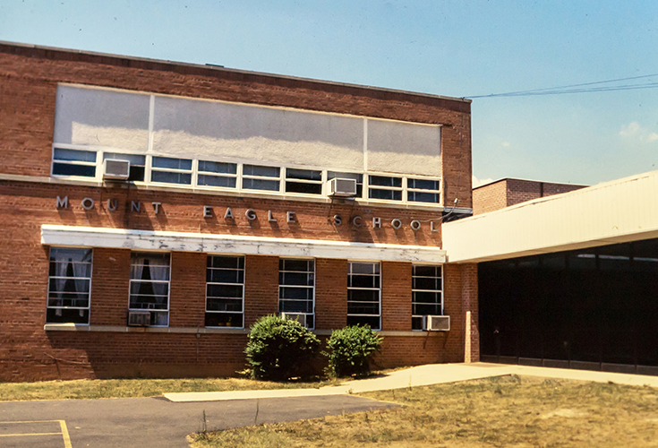 Color photograph of the exterior of Mount Eagle Elementary School showing the classrooms closest to the main entrance. The picture was taken in the late 1980s prior to renovation. Window mounted air conditioning units are affixed to several of the classroom windows.  